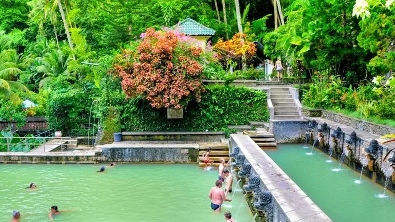 Travelers relaxing at Banjar Hot Spring, North Bali, surrounded by tropical gardens and stone-carved dragon fountains.