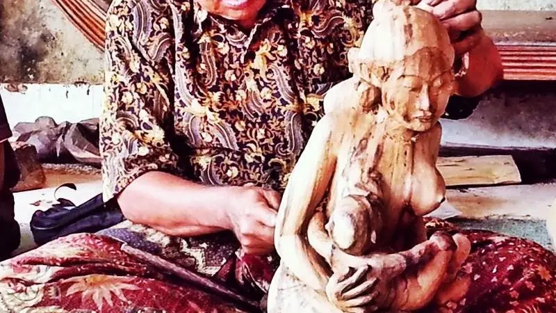 Balinese woodcarver shaping a traditional statue of a mother and child in Mas Village